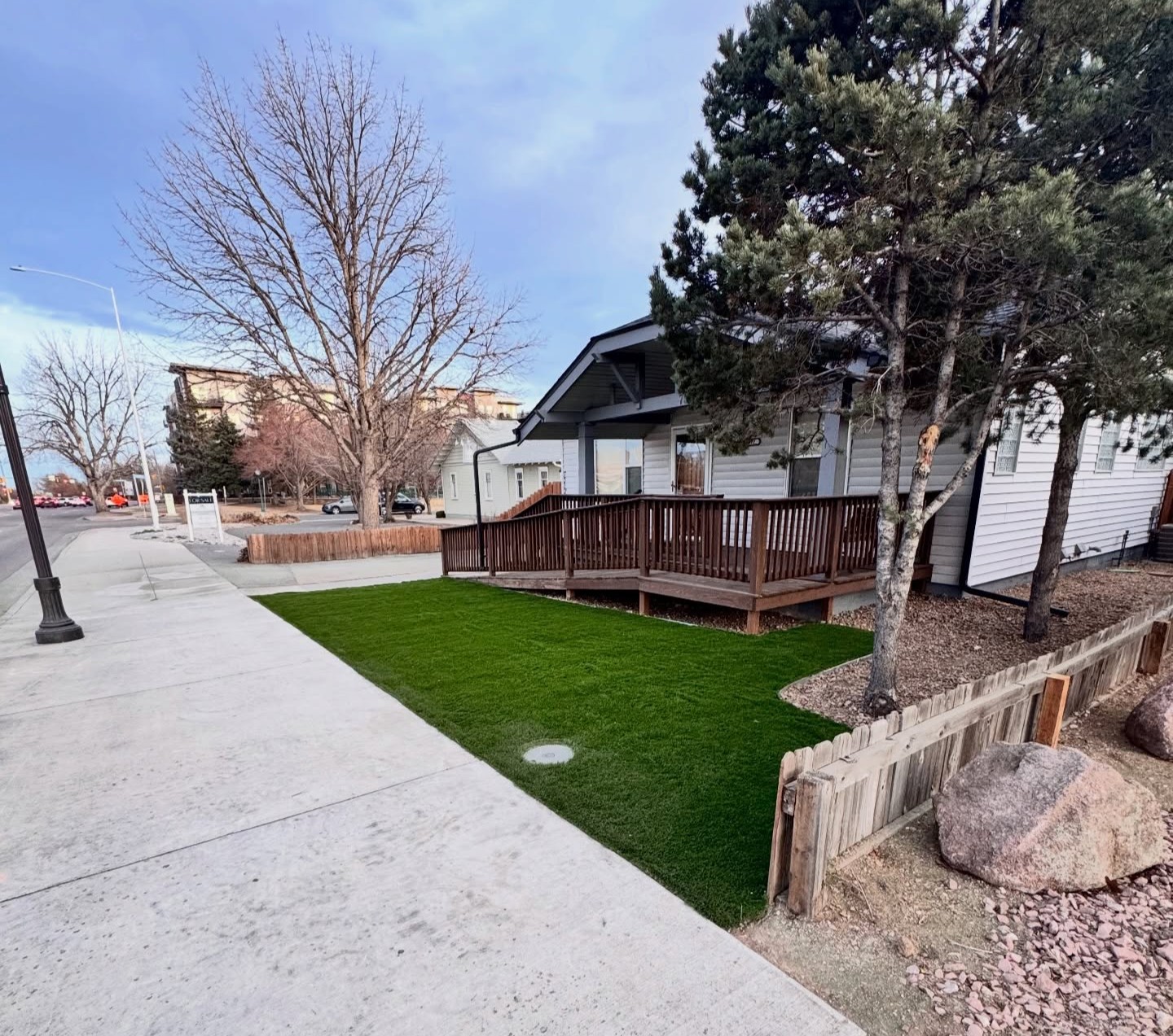 Green lawn beside a house with a wooden deck, trees and rock landscaping